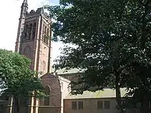 The tower and part of the body of a sandstone church seen from the north between trees