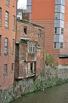 Image 17A 19th-century slum dwelling. The overhang contained privies, whose waste fell straight into the River Medlock below. (from History of Manchester)