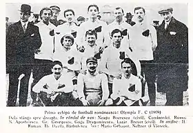 group of 11 men in three rows, sitting, kneeling and standing, dressed in black and white football kit, flanked by 2 men in suits