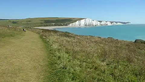 A photograph which illustrates that on Short Cliff above Cuckmere Haven, the Vanguard Way follows a coastal path. The widely known Seven Sisters chalk cliffs are shown in the distance.