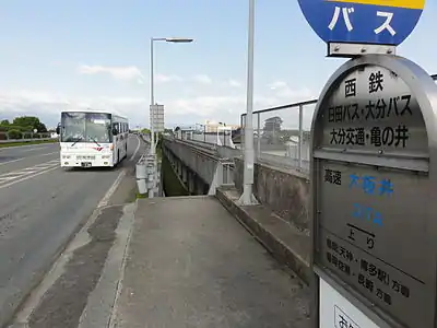 Express bus stop. Note station to the right is at the same level as the highway. The steps descend below the elevated tracks where another flight of steps leads to the station platform.