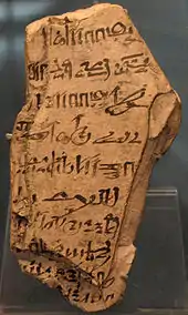 A light-colored stone fragment with hieratic handwriting in black ink scrawled on its surface