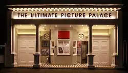 Porticoed façade with two Roman Doric columns on square plinths. Two pairs of double doors flank a small ticket office.