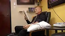 A man reading with an IV in his arm. The tubing is filled with blood