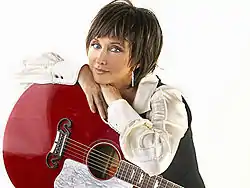 Country music singer Pam Tillis, posing with her arms crossed over top a red acoustic guitar.