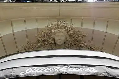 Beaux Arts mascaron with a multitude of flowers around it, above a window of the parfumery of Jacques and Pierre Guerlain, (Avenue des Champs-Élysées no. 68), Paris, designed by architect Charles-Frédéric Méwès and decorated by Bérard Christian, 1912