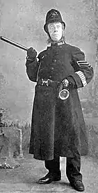 Youngish white man in the uniform of a Victorian British police sergeant, brandishing a truncheon