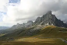 Cloud-covered mountains sit as the backdrop to a green valley below, with a serpentine road running through it.