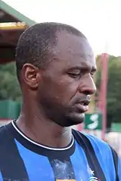 A dark-skinned man wearing a black and blue striped shirt.