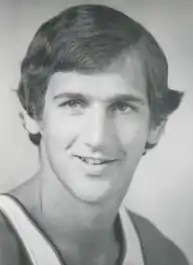 A man with long hair wearing a basketball jersey smiles.