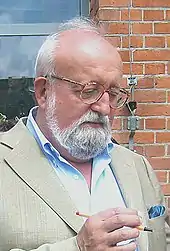 A man with a grey beard: he is wearing glasses and a blue shirt.