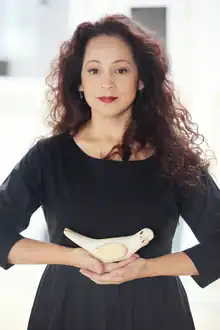 A woman with a neutral expression, wearing a dark dress and holding a model of a dove.