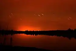 A red sky reflected in a lake at night, with short time-lapse trails of brighter stars