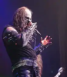 A white man dressed in black holding a microphone.