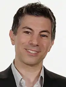 A headshot of a man with dark greying hair smiling at the camera