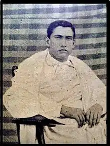 Seated, serious-looking young man dressed in white