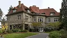 A large house of many windows with white panes, and with a red-checkered roof with many steep sides