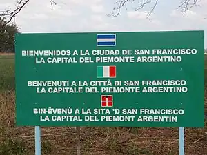 Sign in San Francisco, Córdoba, Argentina; unusually, the Spanish language is indicated by an Argentine flag, while below it is Italian and Piedmontese text with the flags of Italy and Flag of Piedmont.