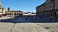 Plaza do Obradoiro as viewed from the Hostal dos Reis Catolicos. The Santiago de Compostela Cathedral is on the left. Large groups of pilgrims clap and celebrate their completion of the Camino de Santigo upon entering the Plaza and congregate in the square, as seen in this image