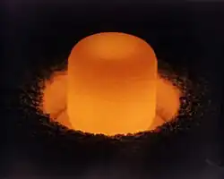 Glowing cylinder of plutonium oxide standing in a circular pit