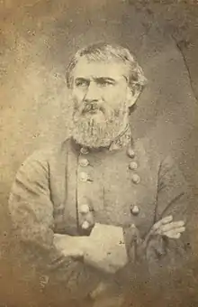 Sepia toned photo shows a frowning, bearded man with his arms crossed. He wears a gray military uniform with two rows of buttons.