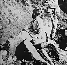 Black-and-white photograph of a bearded man, seated, outside, facing away from the camera.