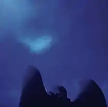 A blue photograph of a sky taken over the shoulders and wings of an angel statue