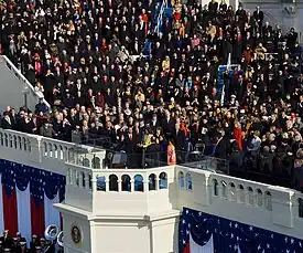 View of a large portion of a large ceremony with visible red, white and blue ornamentation and a crowd of attendees