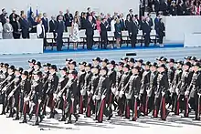 Photograph showing Presidents Macron and Trump and other dignitaries standing in the background reviewing French troops marching in the foreground at the 2017 Bastille Day celebrations in Paris, France