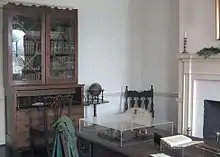 Photography of a library, showing a hutch with books in it and a table with various items on it.