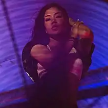 An image of Jhené Aiko posing in blue/purple lighting