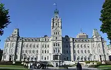 A palace-like building with the flag of Quebec weaving from its central spire