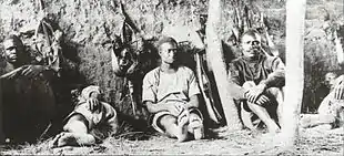 Men sit against a wall, clearly tired. Some are sleeping.