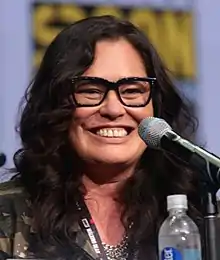 Close-up of a smiling, black-haired woman at a microphone.