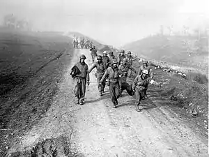 Monochrome photo of soldiers carrying wounded people on a long dirt road