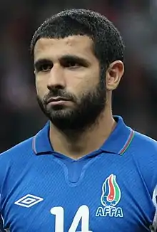 A bearded man in a blue top sits behind a desk at a press conference