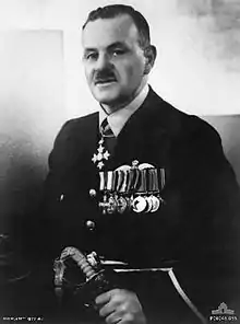 Half-length portrait of a moustachioed man in senior military uniform. He is wearing a group of ten military medals on his breast, with another around his neck and is grasping a sword.