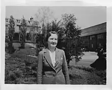 A white woman standing outdoors, wearing a suit jacket and white blouse