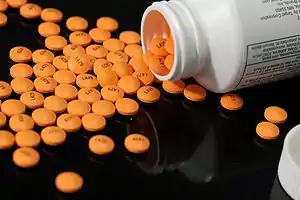 A pill bottle on its side with orange circular tablets spilled out