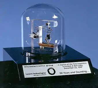 Bell jar covering assembly of plastic and wires, on an engraved plaque commemorating 50 years of the transistor