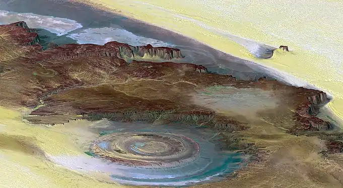 The Richat Structure is a depression in the country of Mauritania, almost 50 km (30 mi) across. It was originally thought to be the impact of a meteorite. Now  it is thought to be a symmetrical uplift (circular anticline or dome) that has been exposed to erosion. In this false-color photo, bedrock is brown, sand is yellow and white, vegetation is green, and salty sediments are blue. (Credit: Landsat 7.)