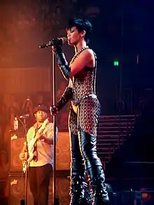  A young woman with black short hair is singing into a microphone on a stand while wearing a leather outfit