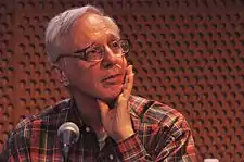 A man wearing a plaid-red shirt speaks into a microphone.