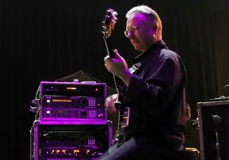 Robert Fripp ergonomically plays electric guitar while sitting in a posture developed through years of application of the Alexander Technique.