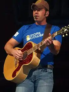 Singer Rodney Atkins, strumming an acoustic guitar while singing into a headset microphone.