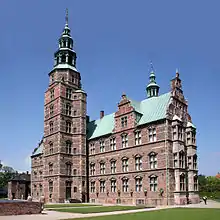 Castle with turrets and spires and walled enclosure, on the tip of a narrow peninsula.