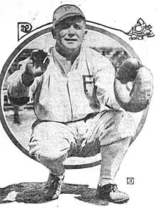 A man in a white baseball uniform with a "P" on the chest and cap is crouched waiting–catch a ball in his catcher's mitt.