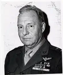 A black-and-white photo of Ross E. Rowell, a white male, in his Marine Corps uniform. There is a map in the background behind him, his ribbons are on the left breast side of his uniform directly above the pocket and he is wearing 2 star general rank insignia on each shoulder of his uniform. Directly above his ribbons he is wearing his Naval Aviator wings.