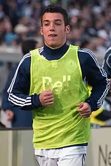 A man running while wearing a green piney over a blue sweatshirt and white shorts.