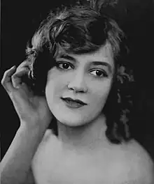 A young smiling white woman with curly hair, one hand behind her ear